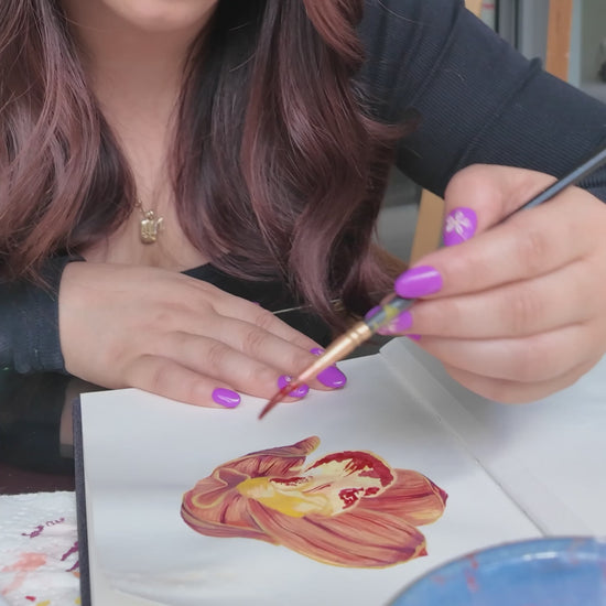 Girl in black top holding a paint brush painting orange orchid flower