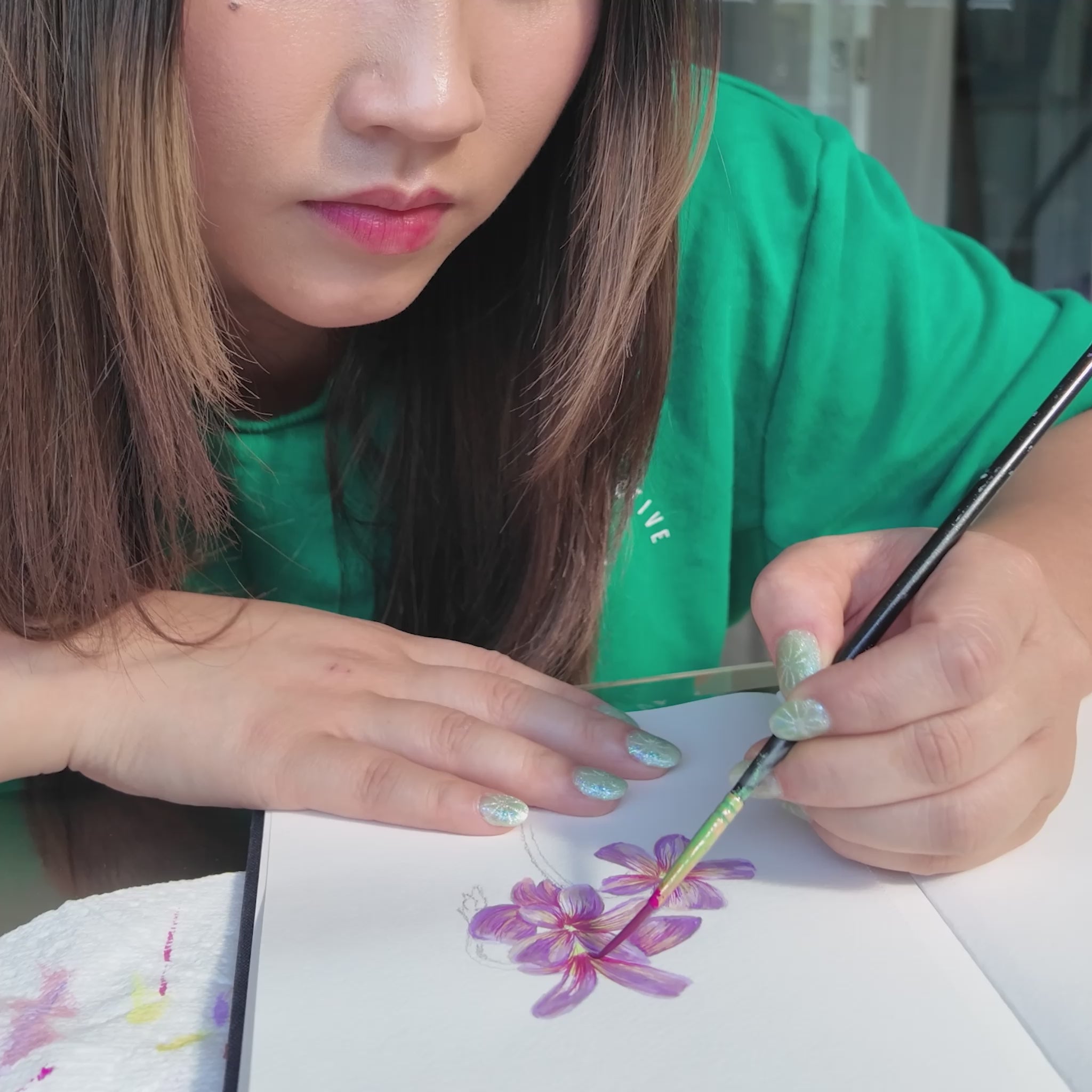 Girl in green top holding a paint brush painting a pink and purple flower