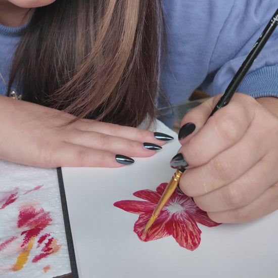 Girl in blue sweater holding a paint brush painting a red and pink flower