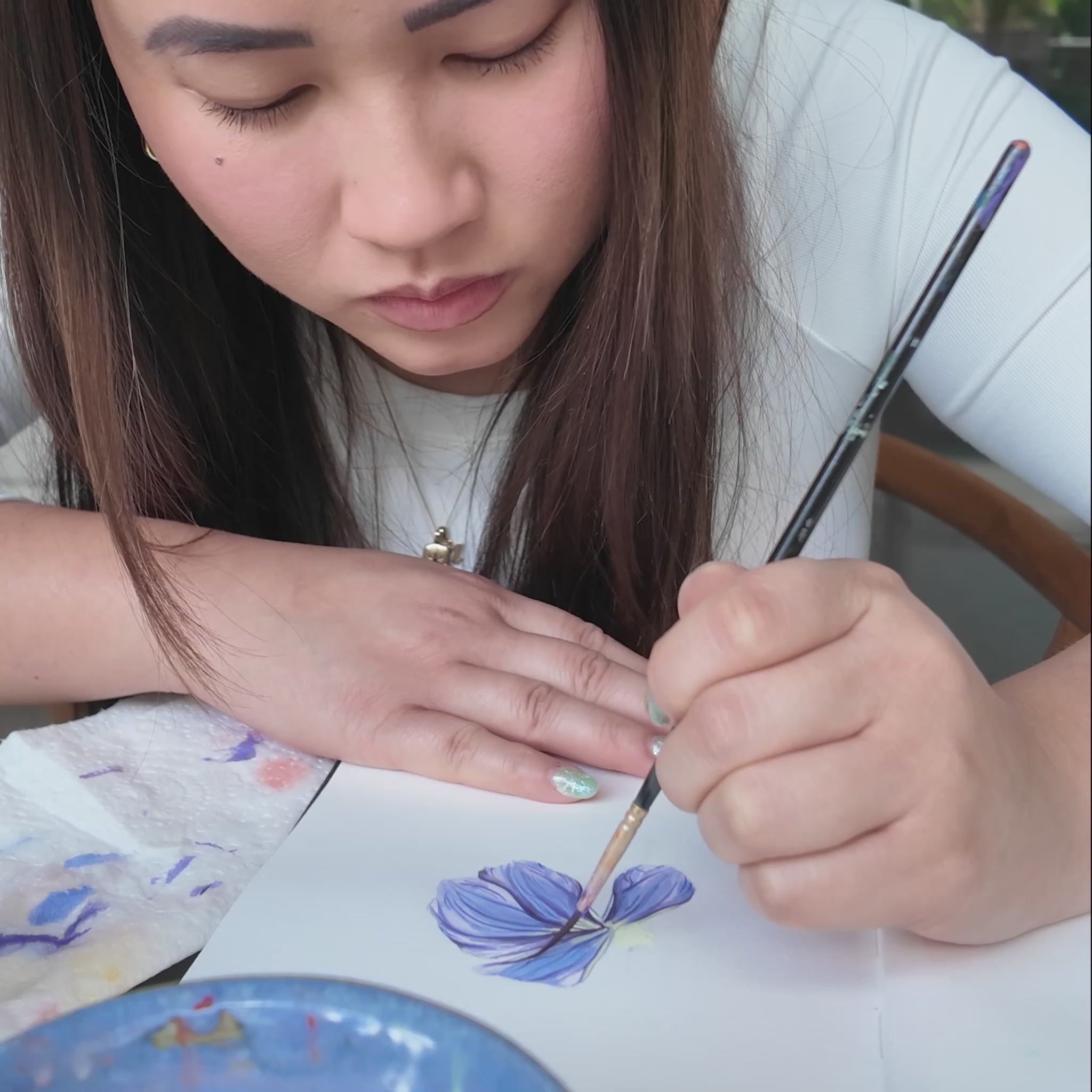 Girl in white top holding a paint brush painting blue dune flower