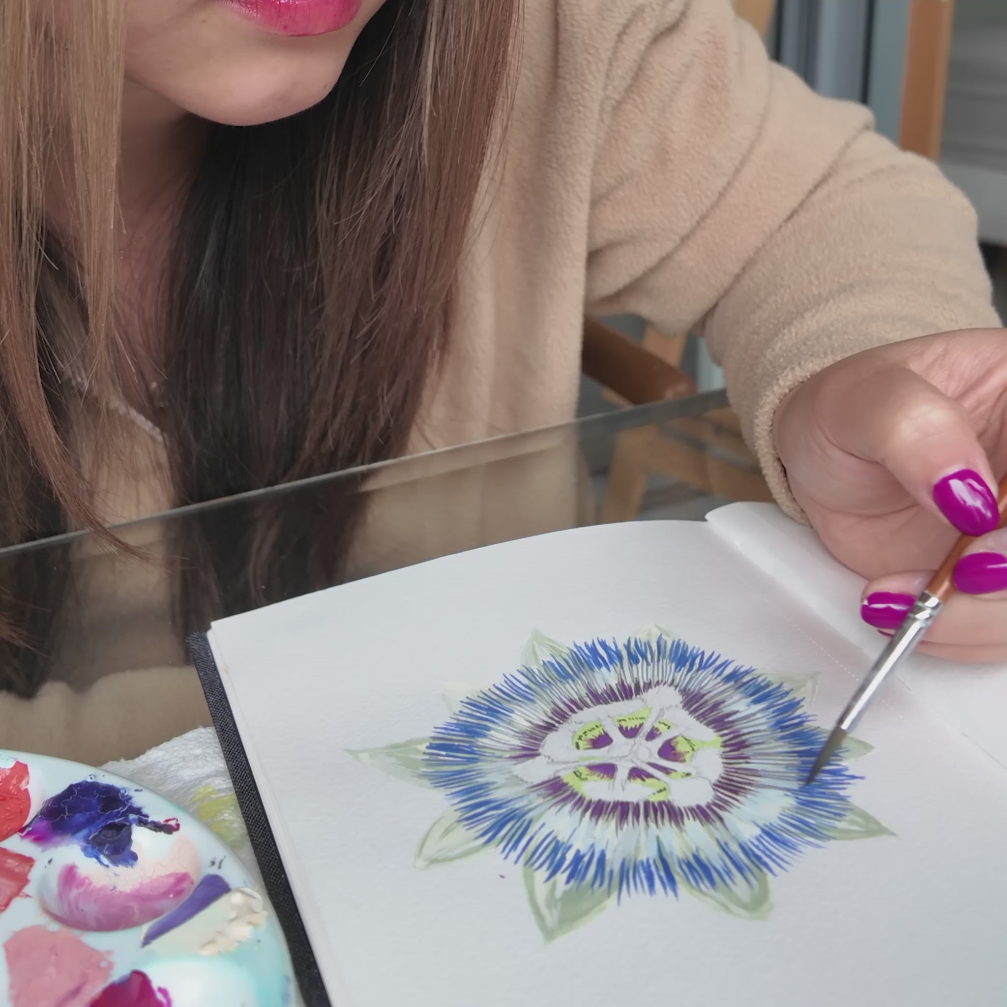 Girl in beige sweater holding a paint brush painting passionfruit flower